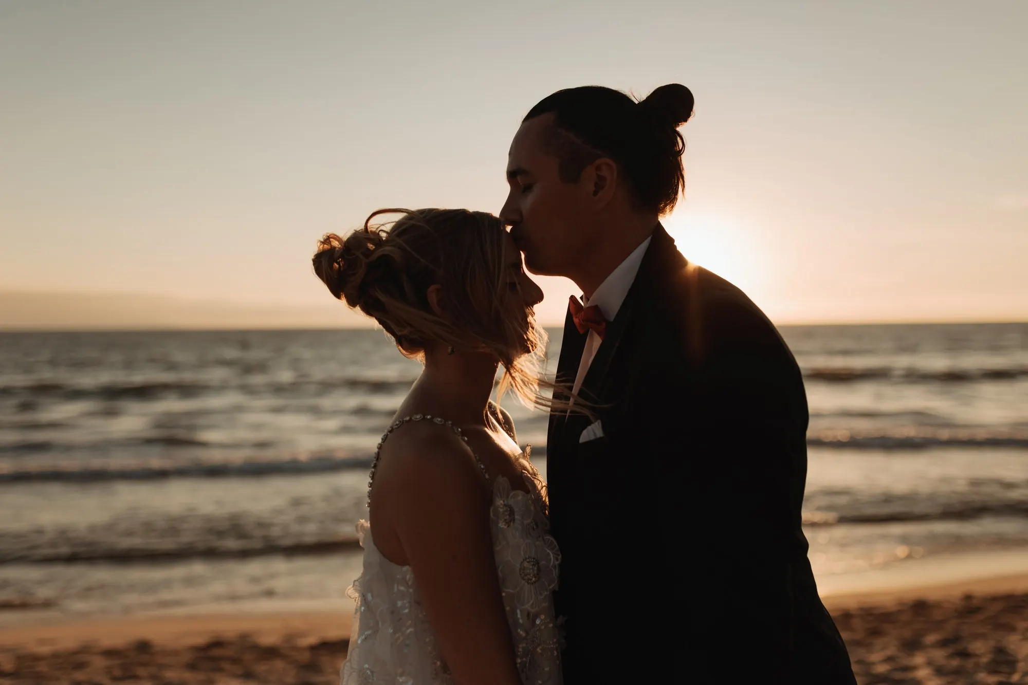 A couple kissing on the sand as the sun drops into the sea